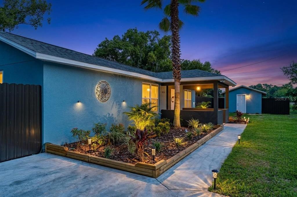A blue house exterior features a landscaped front garden, a palm tree, and illuminated walkways — 21149 LITTLE LAKE THOMAS ROAD, LAND O LAKES, FL