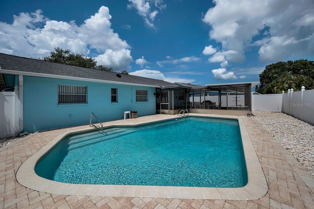 A backyard features a swimming pool with a paver deck and a light blue house — 1614 DALE CIRCLE N, DUNEDIN, FL