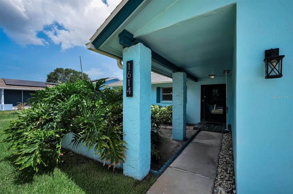 A bright blue house exterior features a covered entryway with stone-textured pillars and a walkway — 1614 DALE CIRCLE N, DUNEDIN, FL