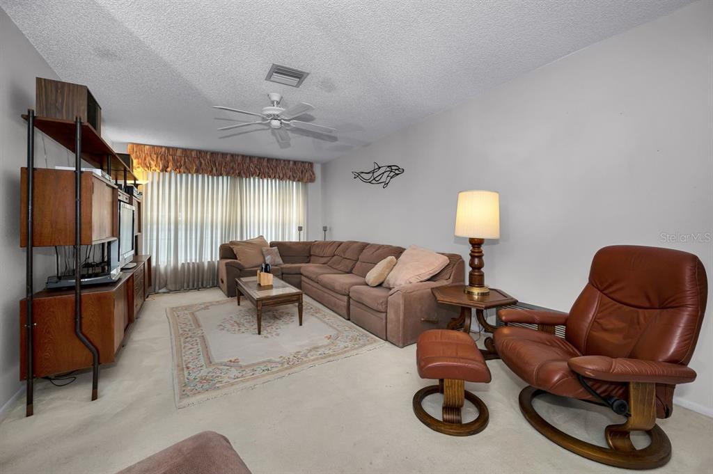 A living room features a brown sectional sofa, a leather recliner, and a wooden wall unit — 1614 DALE CIRCLE N, DUNEDIN, FL