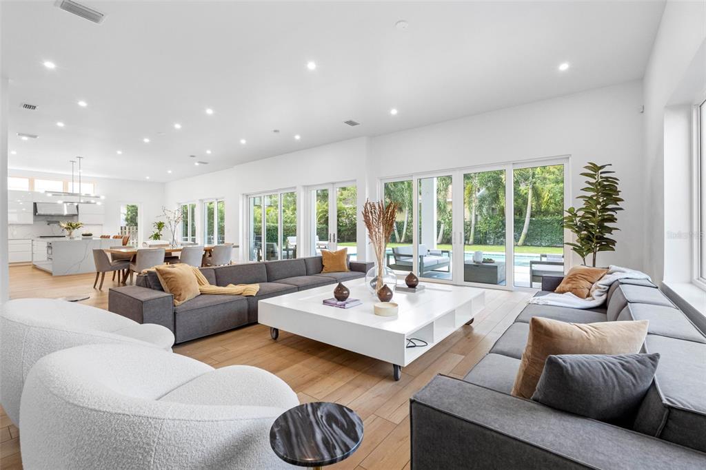 A bright, open-concept living room features gray sectional sofas, a large white coffee table, and sliding glass doors — 3208 W LAWN AVENUE, TAMPA, FL