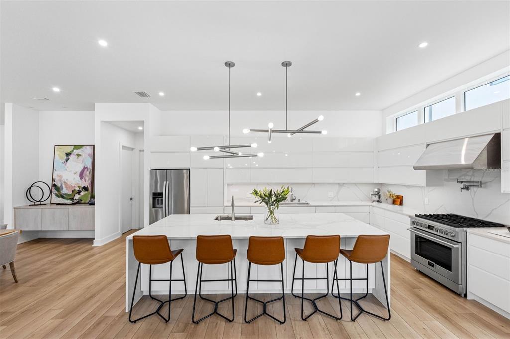 A modern kitchen features white cabinetry, a large marble-topped island, and five brown bar stools — 3208 W LAWN AVENUE, TAMPA, FL