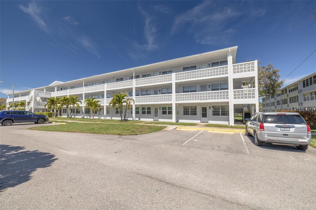 A three-story white apartment building with exterior walkways and parking spaces in the foreground — 1001 77TH AVENUE N UNIT 112, ST PETERSBURG, FL
