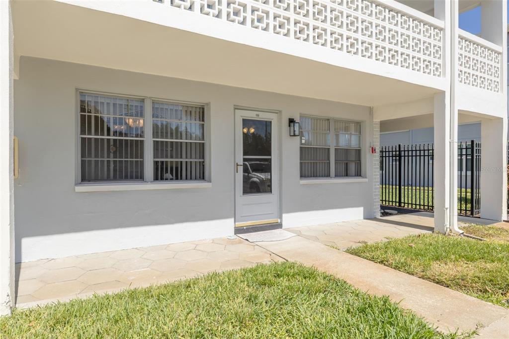A ground-level apartment entrance features a white door, windows, and a paved patio area — 1001 77TH AVENUE N UNIT 112, ST PETERSBURG, FL