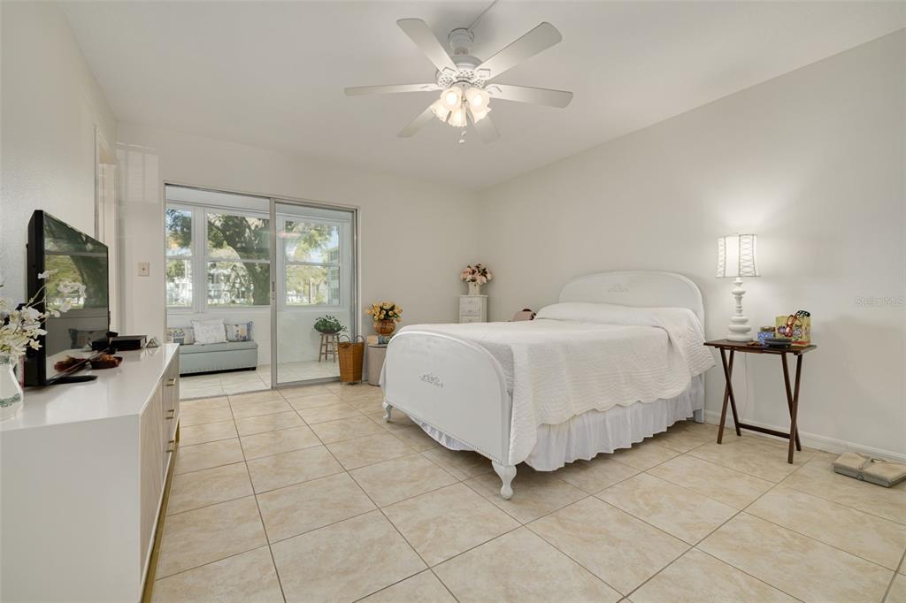 A bedroom with tile flooring, a white bed, a ceiling fan, and a sliding glass door — 1001 77TH AVENUE N UNIT 112, ST PETERSBURG, FL