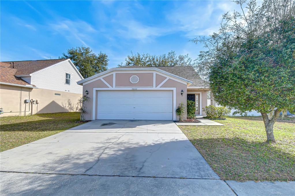 A single-story house with a white garage door, tan stucco exterior, and a front lawn — 24640 SIENA DRIVE, LUTZ, FL