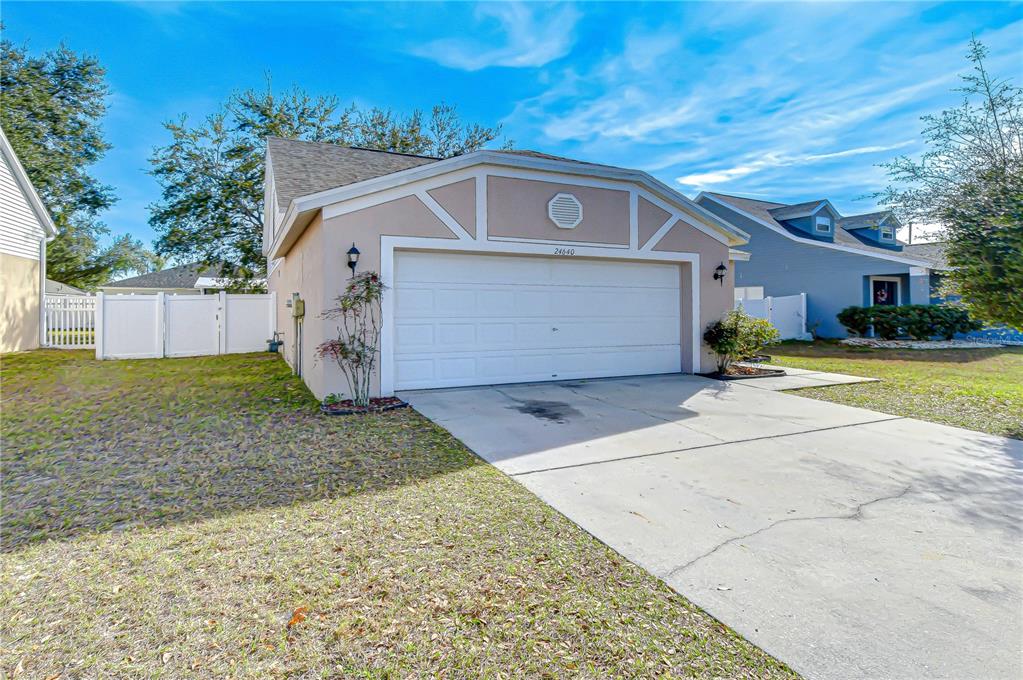 A beige house exterior features a two-car garage, a concrete driveway, and a white fence — 24640 SIENA DRIVE, LUTZ, FL