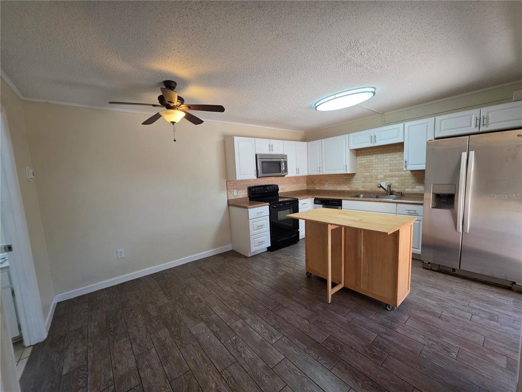 A kitchen features white cabinets, stainless steel appliances, a wooden island, and wood-look tile flooring — 3824 SAXON DRIVE, NEW SMYRNA BEACH, FL