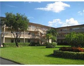 A multi-story apartment building with balconies stands behind a large green lawn and landscaping — 320 Fanshaw H # 320, Boca Raton FL 33434, BOCA RATON, FL