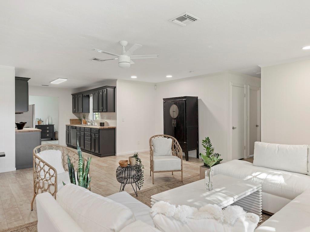 A bright open-concept living room and kitchen featuring white sofas, dark cabinetry, and light flooring — 8530 8th Street, Vero Beach FL 32968, VERO BEACH, FL