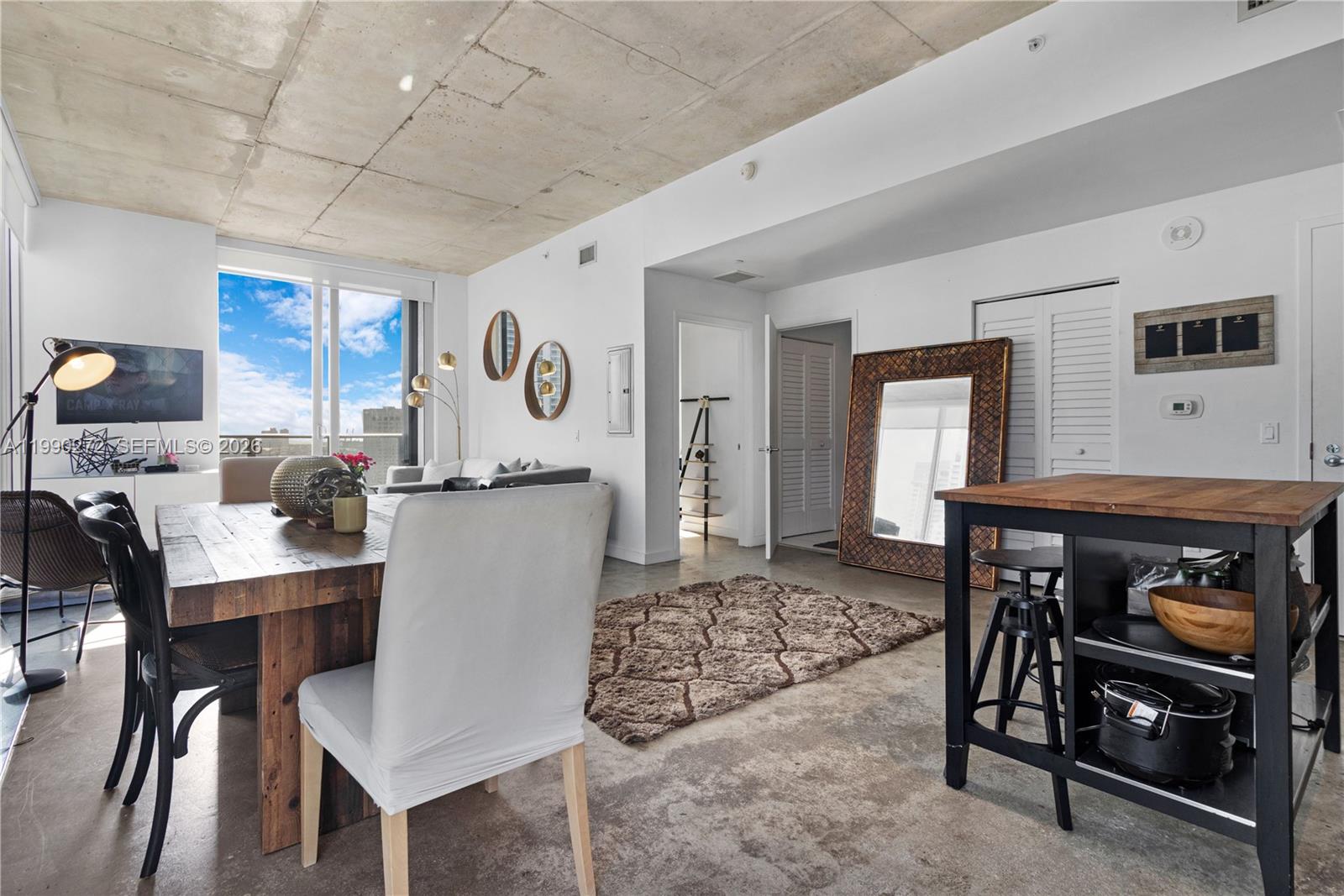 An open-concept living and dining area features a concrete ceiling, concrete floors, and large windows — 151 SE 1st St # 2802, Miami FL 33131, MIAMI, FL
