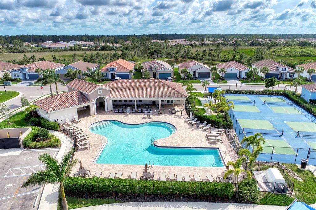 An aerial view shows a community swimming pool, patio, and tennis courts near residential homes — 620 NASTURTIUM COURT, NOKOMIS, FL