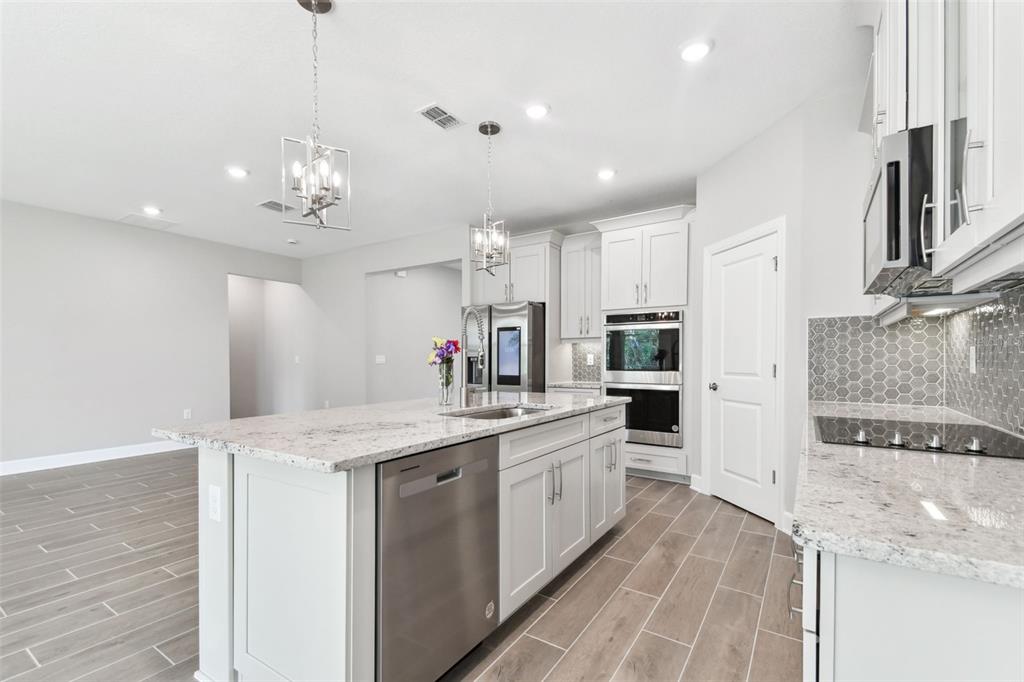 A modern kitchen features white cabinets, granite countertops, stainless steel appliances, and wood-look tile flooring — 620 NASTURTIUM COURT, NOKOMIS, FL