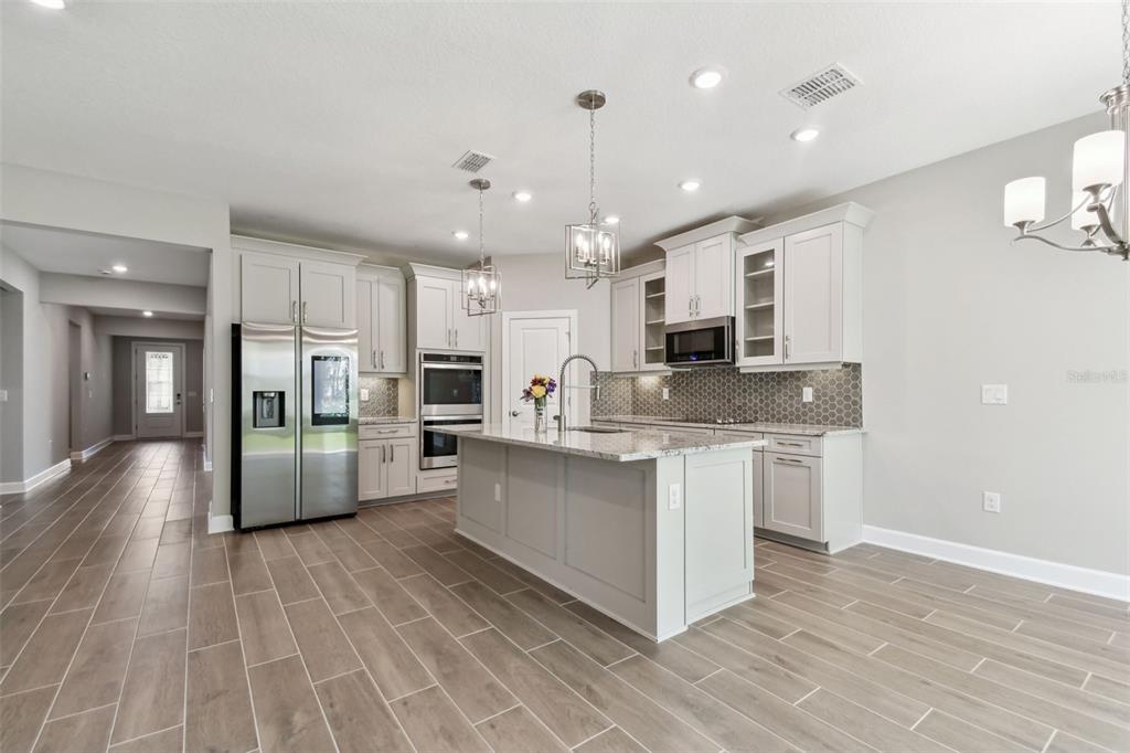 A modern kitchen features light gray cabinetry, a central island, stainless steel appliances, and tile flooring — 620 NASTURTIUM COURT, NOKOMIS, FL