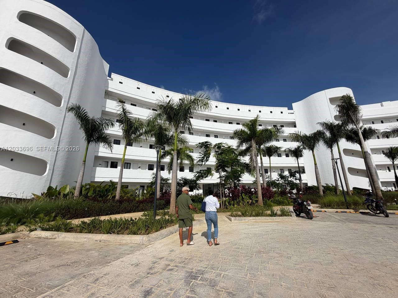 A white, multi-story curved building stands behind a paved courtyard with palm trees — 1 Cana Rock # 215, FL
