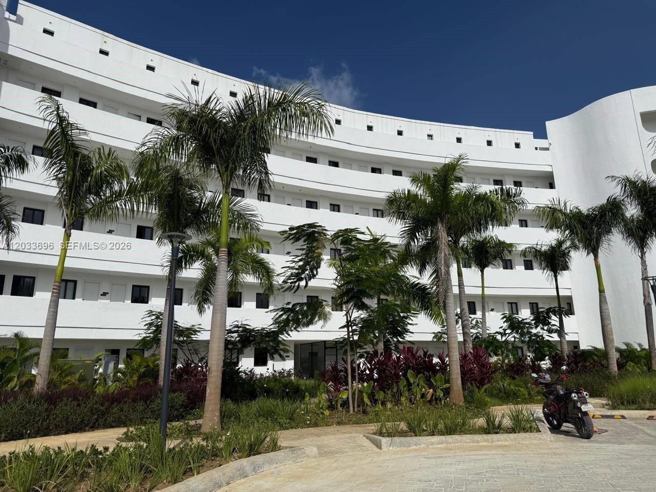 A multi-story white curved apartment building stands behind palm trees and a paved driveway — 1 Cana Rock # 215, FL