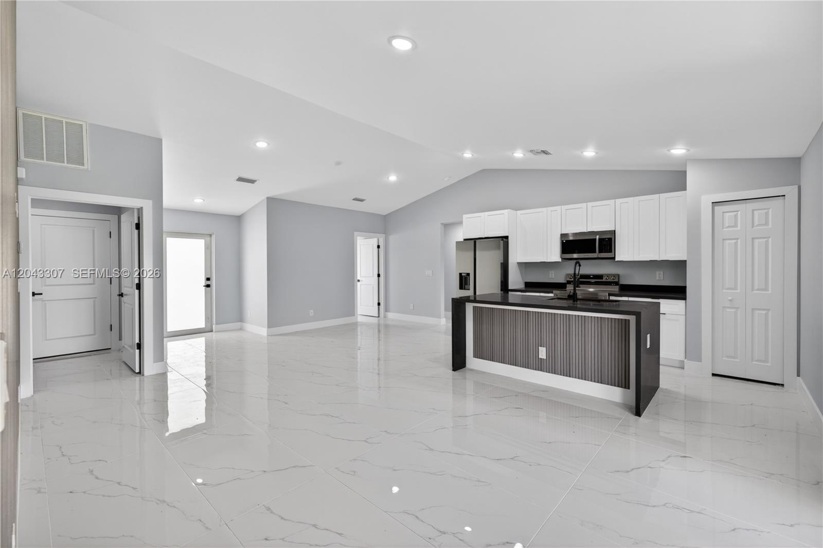 A modern kitchen with a dark island and white cabinets sits in an open-concept room — 702 carbon st, Lehigh Acres FL 33974, LEHIGH ACRES, FL