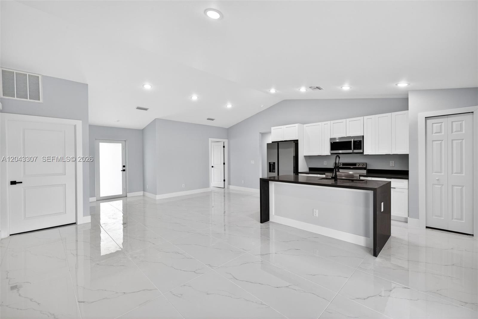 A modern kitchen with white cabinets and a dark island sits in an open-concept room — 702 carbon st, Lehigh Acres FL 33974, LEHIGH ACRES, FL