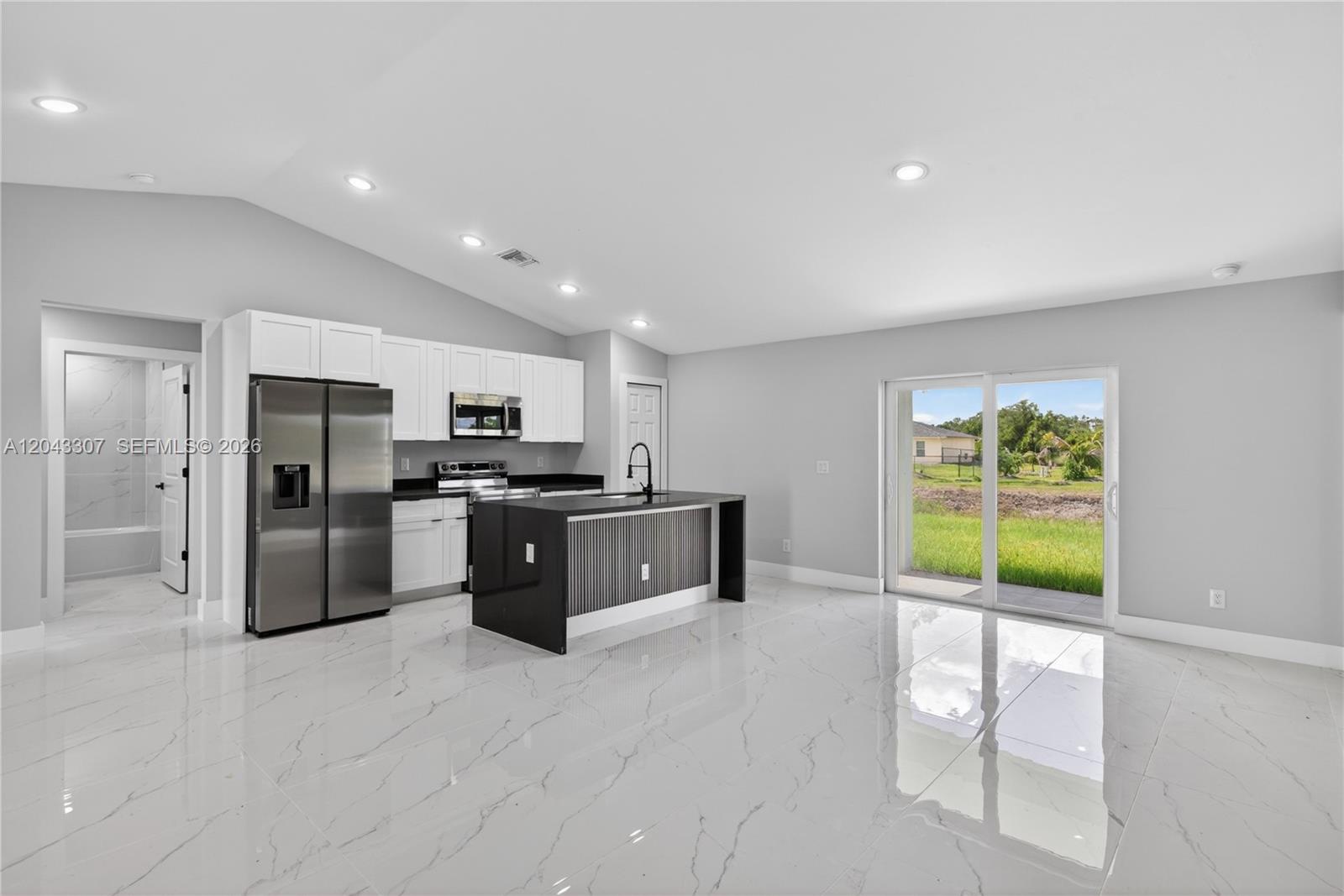 A modern kitchen features white cabinets, a black island, and white marble-look tile flooring — 702 carbon st, Lehigh Acres FL 33974, LEHIGH ACRES, FL