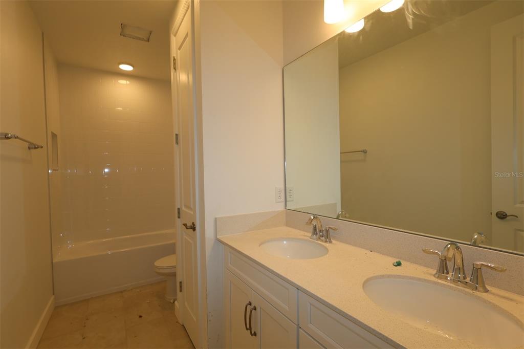 A white kitchen features a large island, quartz countertops, and unfinished cabinetry — 3850 WOLVES CREEK PLACE, APOPKA, FL