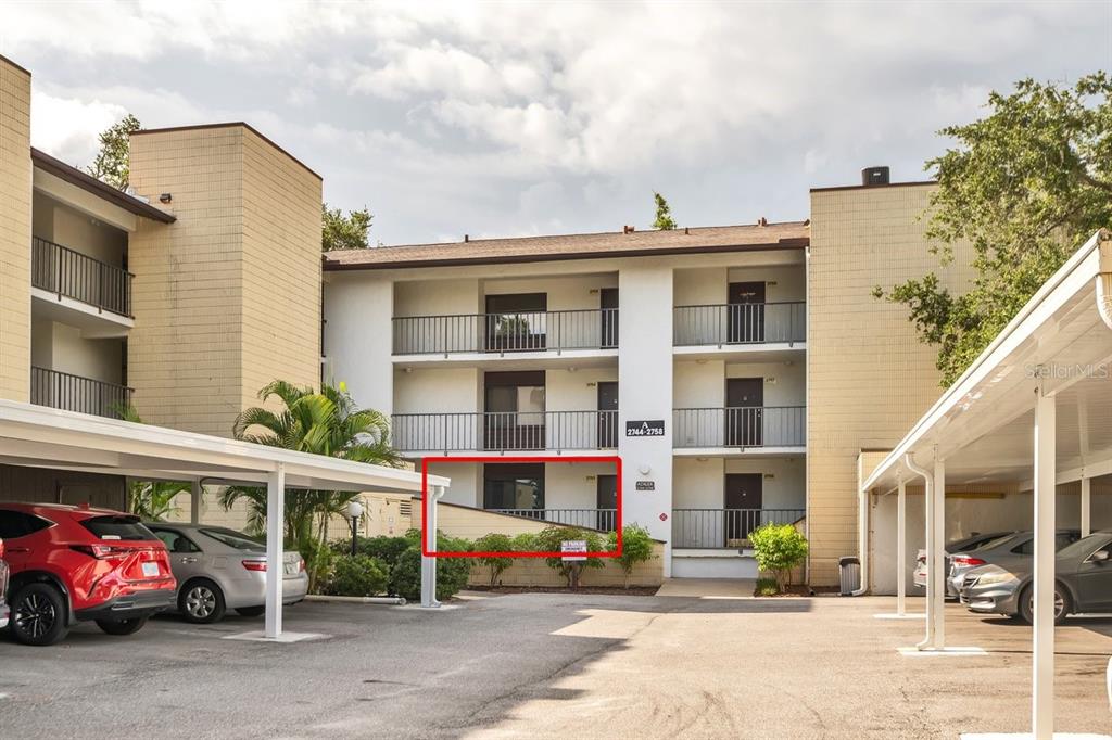 The exterior of a three-story apartment building features a red-outlined ground-floor unit and parking — 2753 ORCHID OAKS DRIVE UNIT 104, SARASOTA, FL