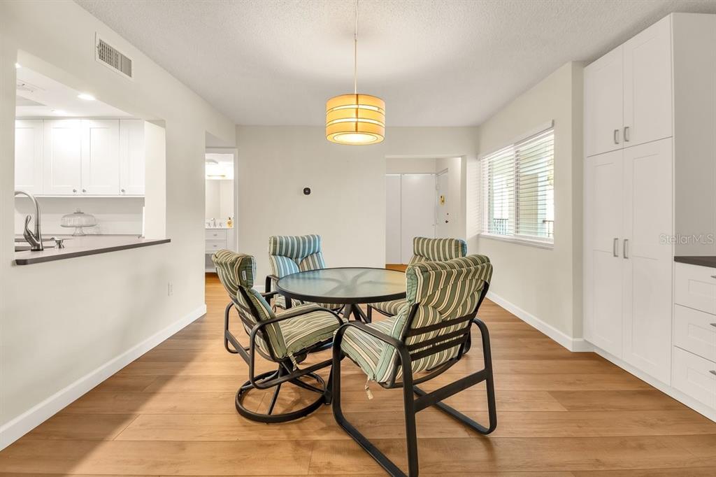 A dining area features a glass-top table, striped chairs, light wood flooring, and white cabinetry — 2753 ORCHID OAKS DRIVE UNIT 104, SARASOTA, FL