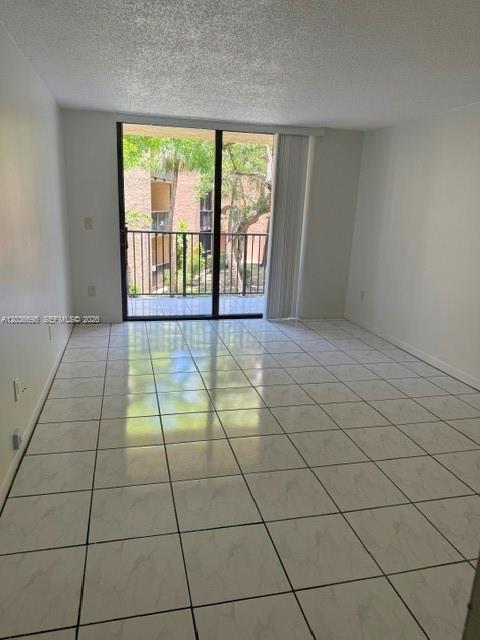 An empty room with white tile flooring and a sliding glass door leading to a balcony — 14221 N Kendall Dr # 211C, Miami FL 33186, MIAMI, FL