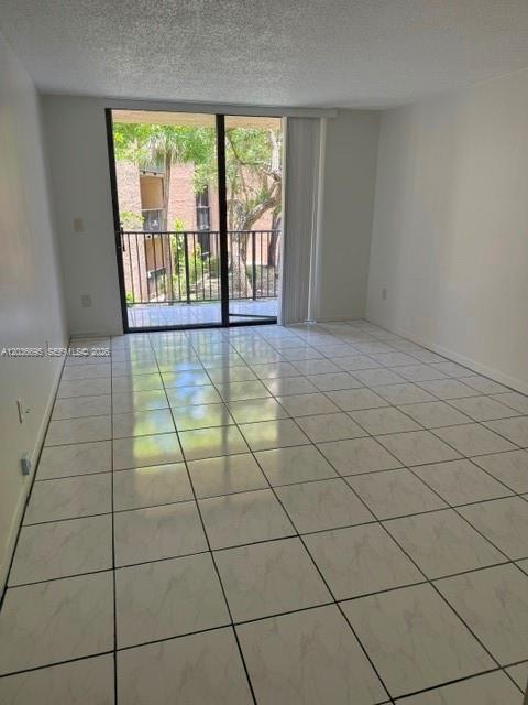 An empty room with white tile flooring and a sliding glass door leading to a balcony — 14221 N Kendall Dr # 211C, Miami FL 33186, MIAMI, FL