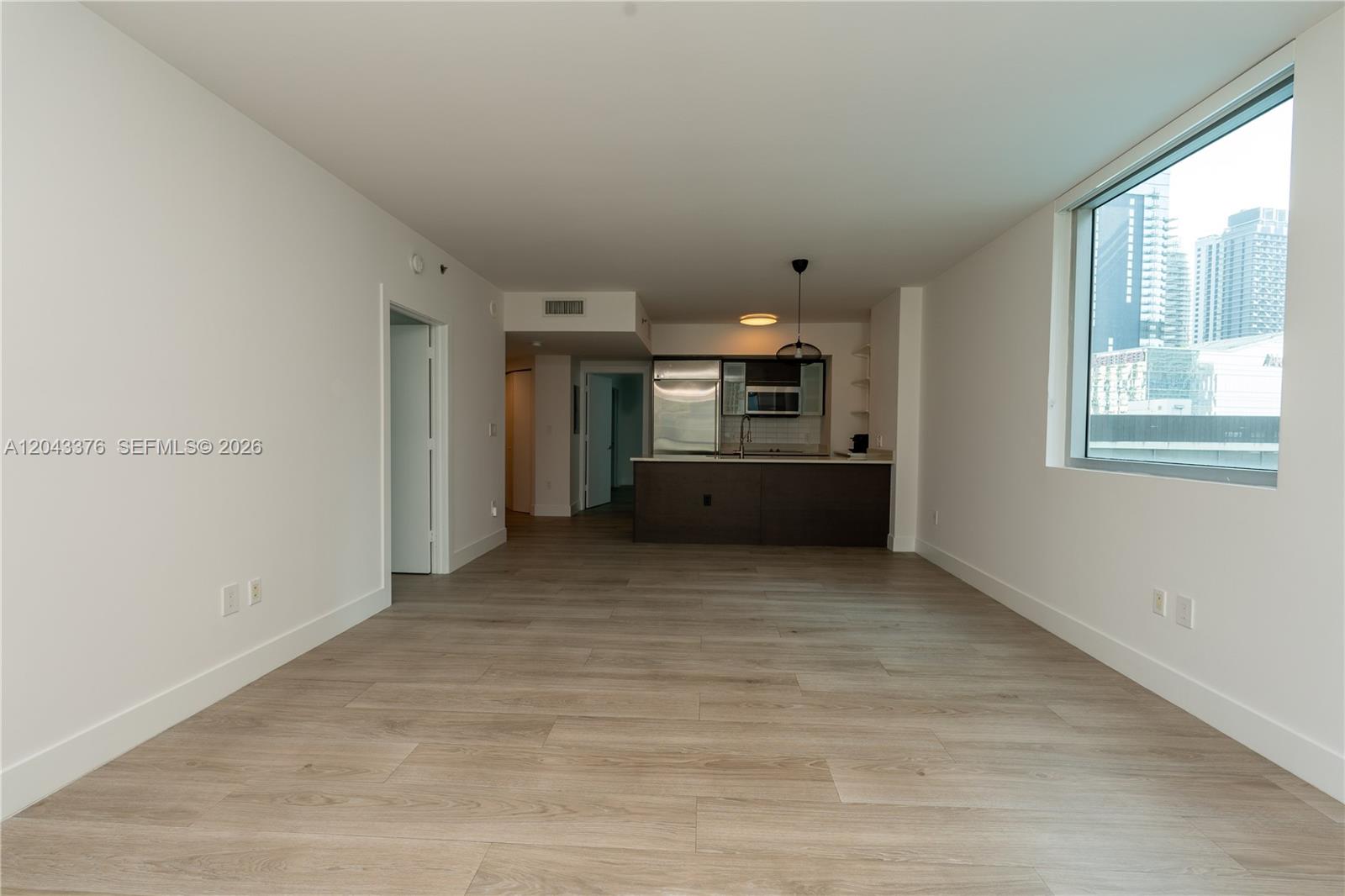 An unfurnished living area features light wood-look flooring, white walls, and an open kitchen — 500 Brickell Ave # 1407, Miami FL 33131, MIAMI, FL