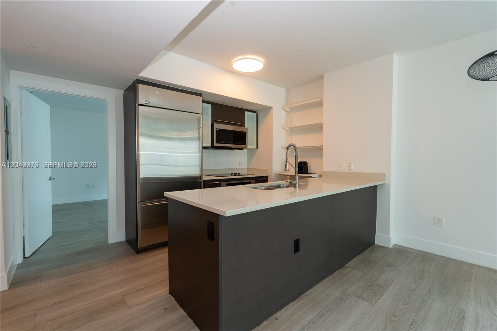 A modern kitchen features dark cabinetry, stainless steel appliances, and a white quartz island countertop — 500 Brickell Ave # 1407, Miami FL 33131, MIAMI, FL