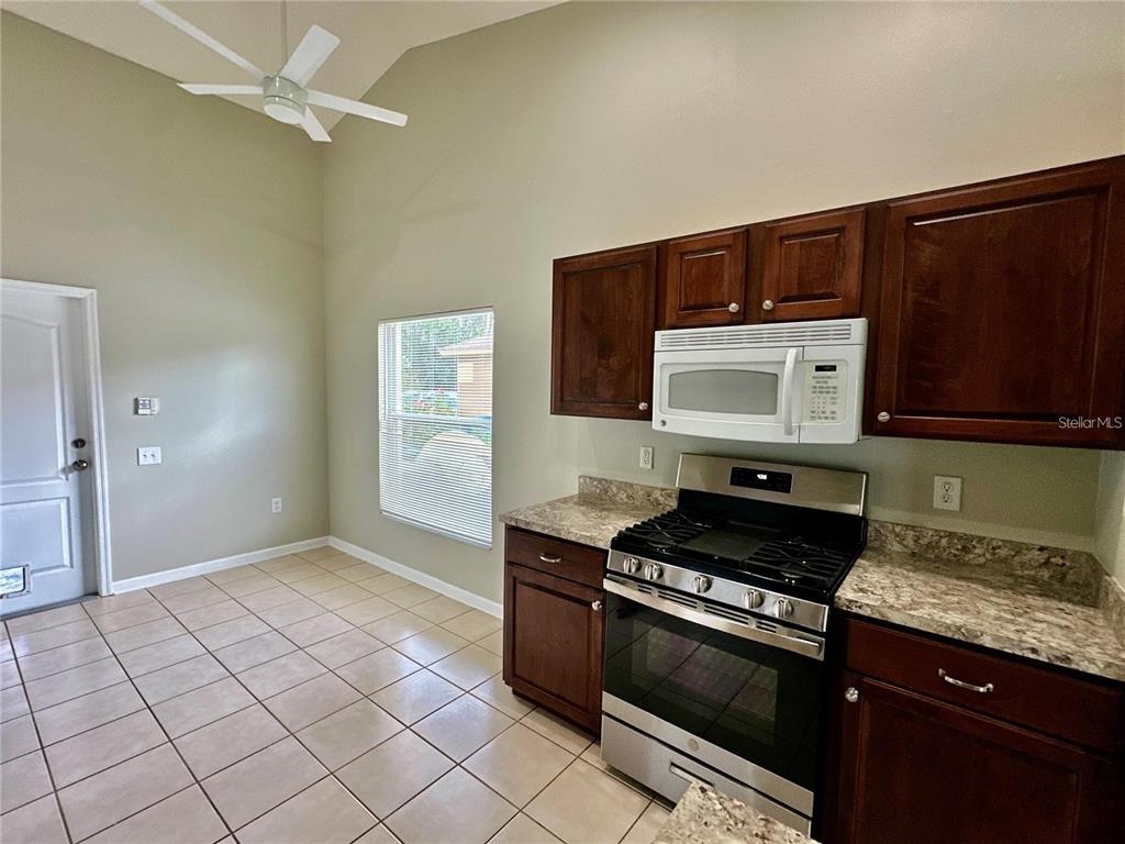 A kitchen features dark wood cabinets, stainless steel appliances, and tile flooring under a vaulted ceiling — 30747 BURLEIGH DRIVE, WESLEY CHAPEL, FL