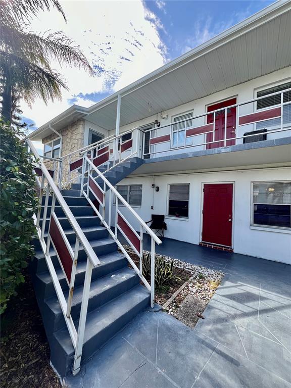 An exterior view of a two-story apartment building with a concrete staircase and red doors — 5920 18TH STREET N UNIT 14, ST PETERSBURG, FL