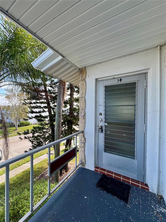 A covered balcony with a gray door, metal railing, and a view of trees and street — 5920 18TH STREET N UNIT 14, ST PETERSBURG, FL