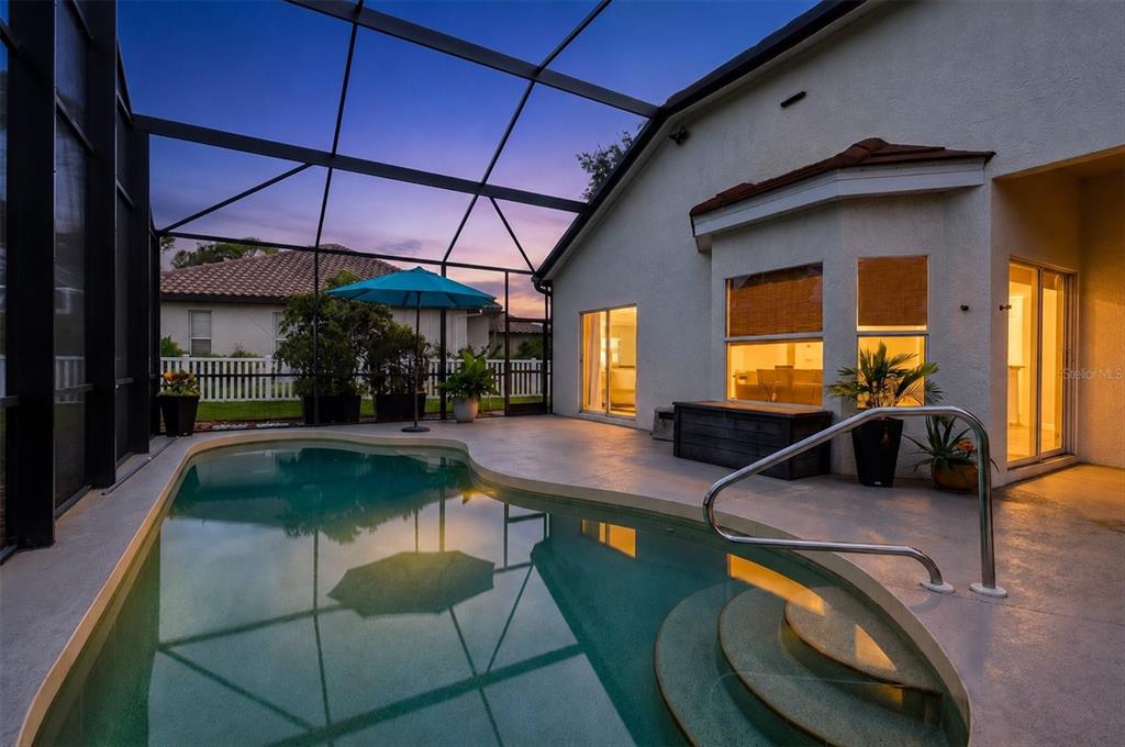 A screened-in patio features a swimming pool with steps and a blue umbrella at dusk — 1059 TRUMAN STREET, NOKOMIS, FL