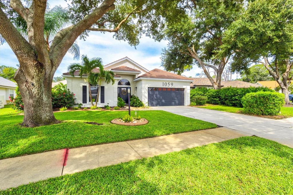 A single-story house with a gray garage, white stucco exterior, and large trees in front — 1059 TRUMAN STREET, NOKOMIS, FL