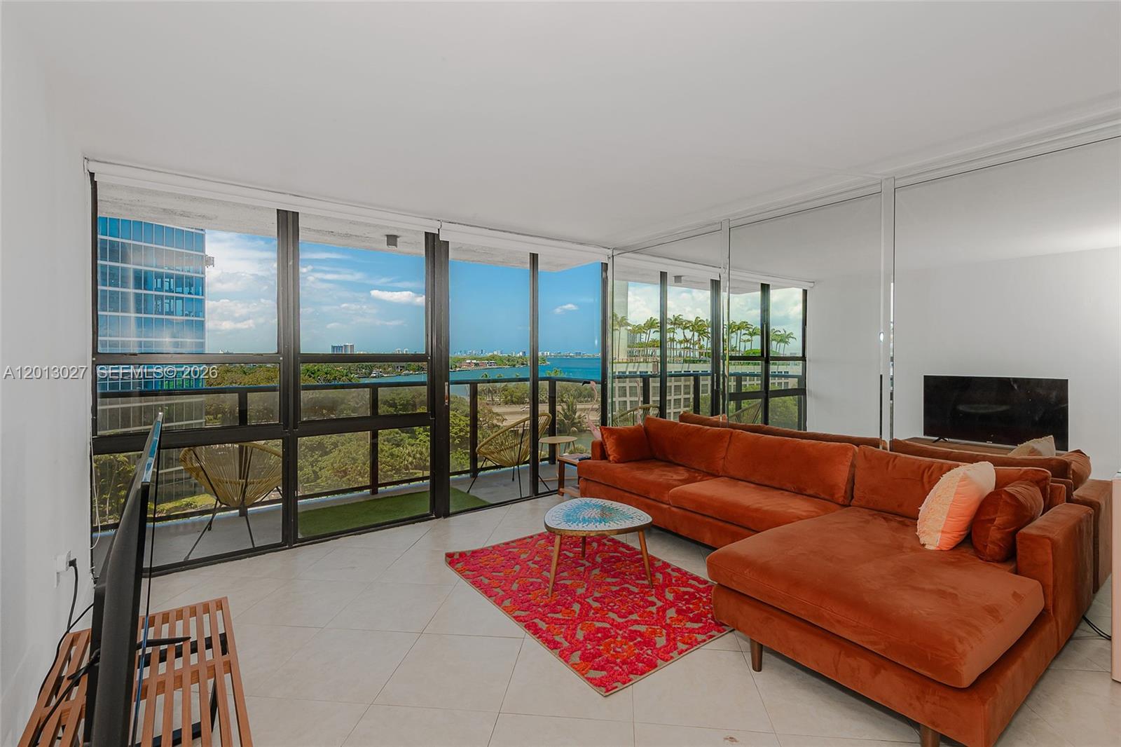 A living room features a large orange sectional, a patterned rug, and floor-to-ceiling windows — 600 NE 36th St # 706, Miami FL 33137, MIAMI, FL