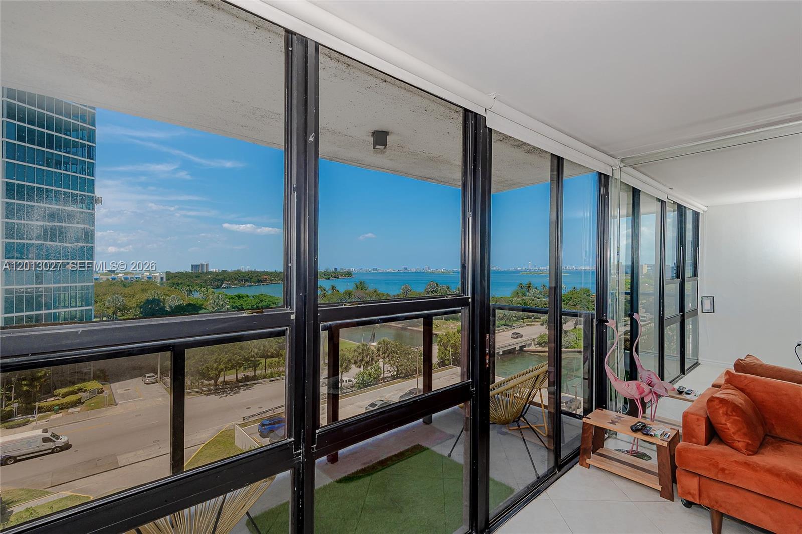 A living room with floor-to-ceiling windows overlooks a balcony, a road, and a bay — 600 NE 36th St # 706, Miami FL 33137, MIAMI, FL