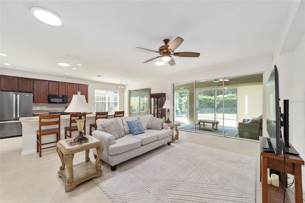 An open-concept living room and kitchen featuring tile floors, a ceiling fan, and sliding doors — 9395 SW 66TH LOOP, OCALA, FL