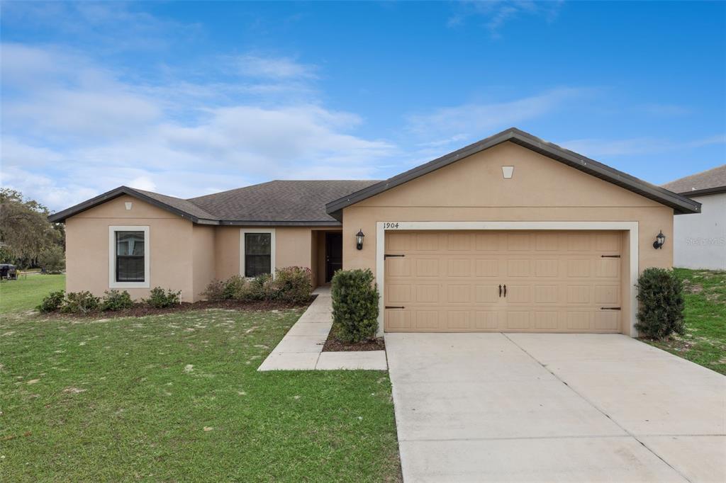 A single-story house with a tan stucco exterior and a two-car garage — 1904 PIEDMONT COURT, MASCOTTE, FL