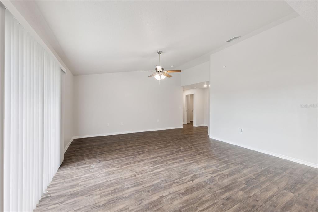 An empty living room features wood-look flooring, white walls, and a ceiling fan — 1904 PIEDMONT COURT, MASCOTTE, FL