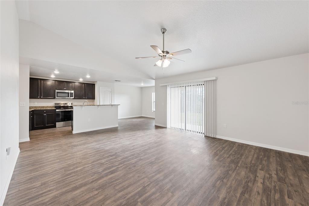 An open-concept living area with wood-look flooring, a ceiling fan, and an adjacent kitchen — 1904 PIEDMONT COURT, MASCOTTE, FL