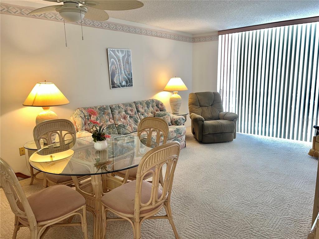A living and dining area features a floral sofa, glass-topped table, and beige carpeting — 519 ALBEE FARM ROAD UNIT 210, VENICE, FL