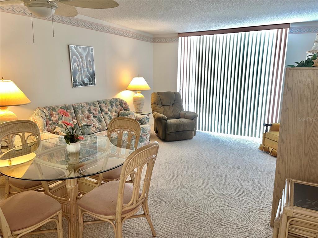 A living and dining area features a floral sofa, glass table, and a recliner — 519 ALBEE FARM ROAD UNIT 210, VENICE, FL