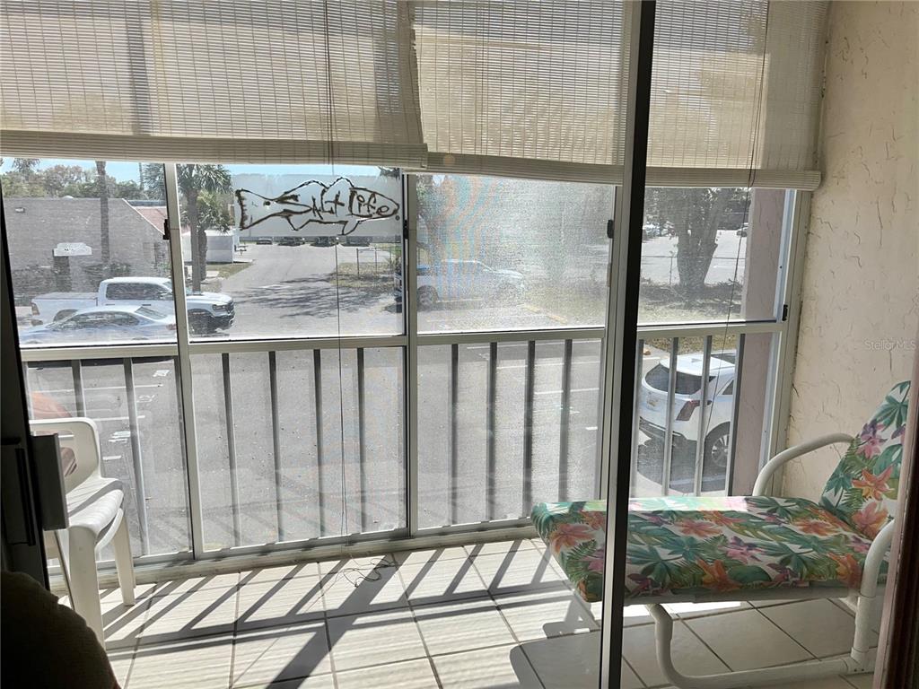 A tiled balcony features a floral lounge chair, a white plastic chair, and sliding glass doors — 519 ALBEE FARM ROAD UNIT 210, VENICE, FL