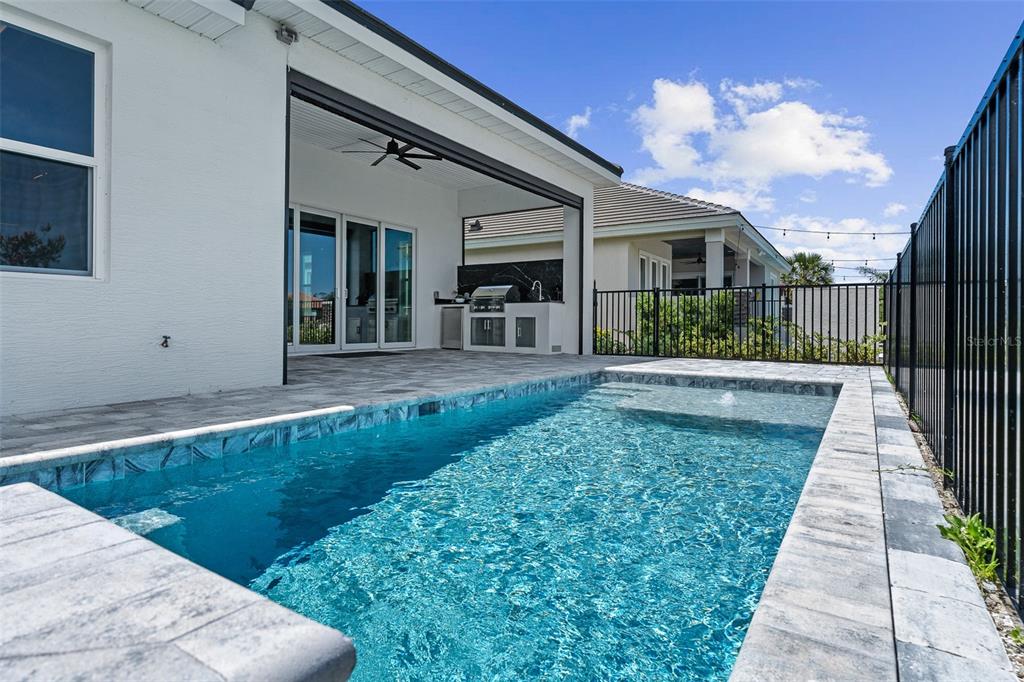 A backyard patio features a covered outdoor kitchen, a swimming pool, and a black fence — 120 DEL PALMA DRIVE, PALM COAST, FL