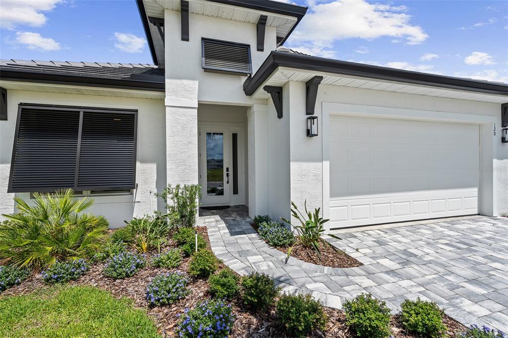 A modern white house exterior features a paved walkway, a garage, and landscaped garden beds — 120 DEL PALMA DRIVE, PALM COAST, FL