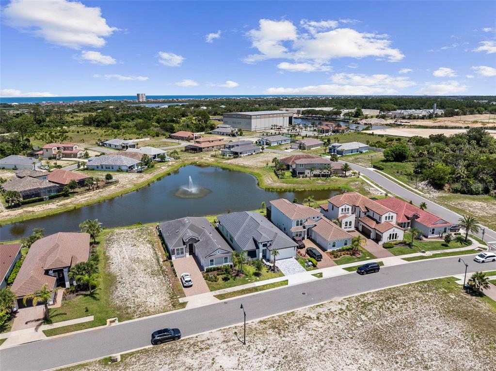 An aerial view shows a suburban neighborhood with houses surrounding a pond with a fountain — 120 DEL PALMA DRIVE, PALM COAST, FL
