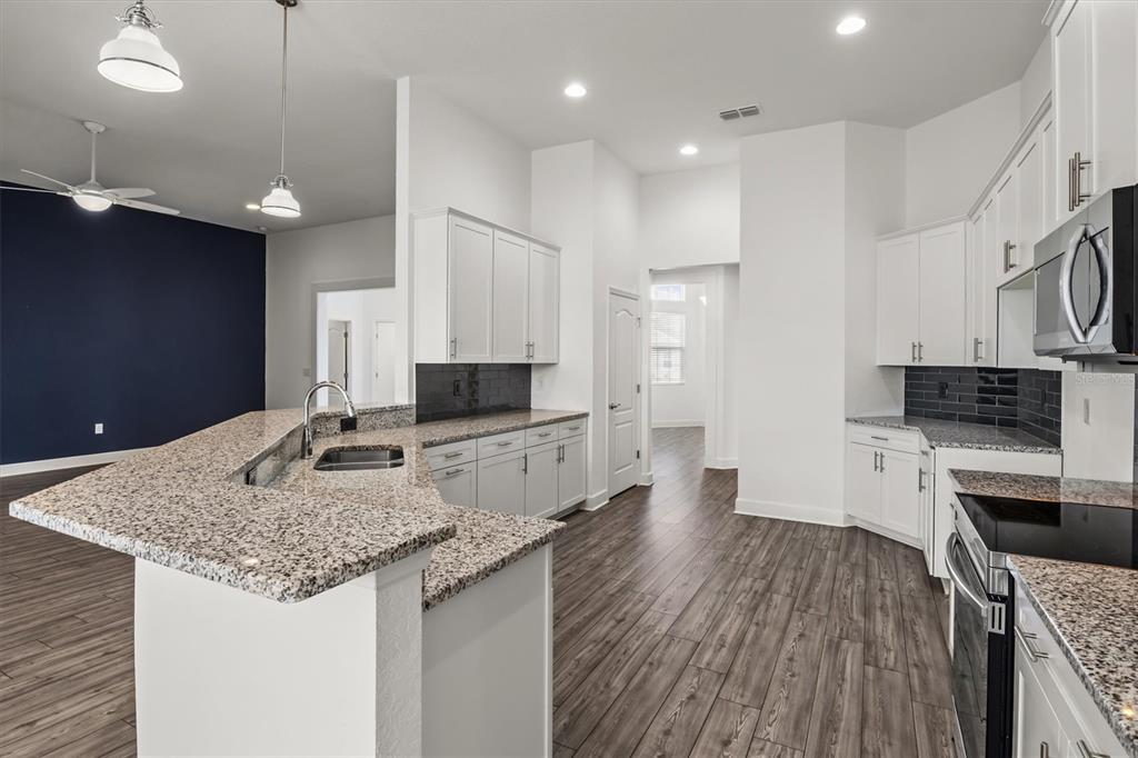 A kitchen features white cabinets, granite countertops, a dark tile backsplash, and wood-look flooring — 530 SANCTUARY BOULEVARD, WINTER HAVEN, FL