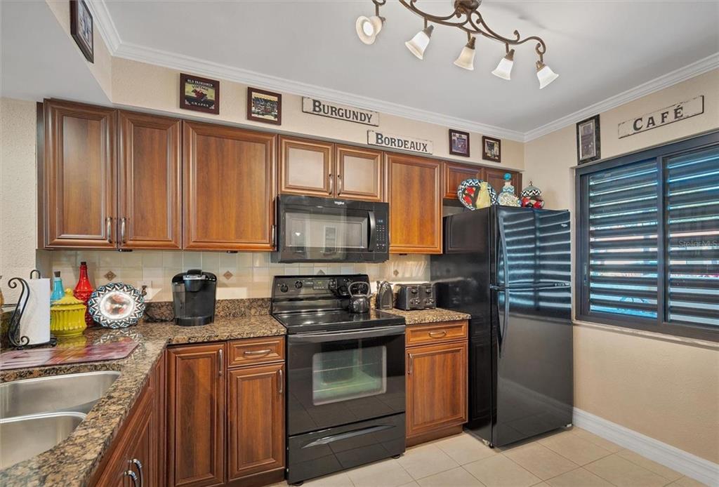 A kitchen with dark wood cabinets, a glass block breakfast table, and tile flooring — 5231 LAKE VILLAGE DRIVE UNIT 27, SARASOTA, FL