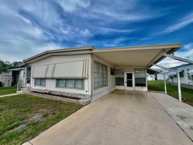 A single-story mobile home with a carport and metal awnings under a cloudy sky — 10920 INDEPENDENCE DRIVE, PORT RICHEY, FL